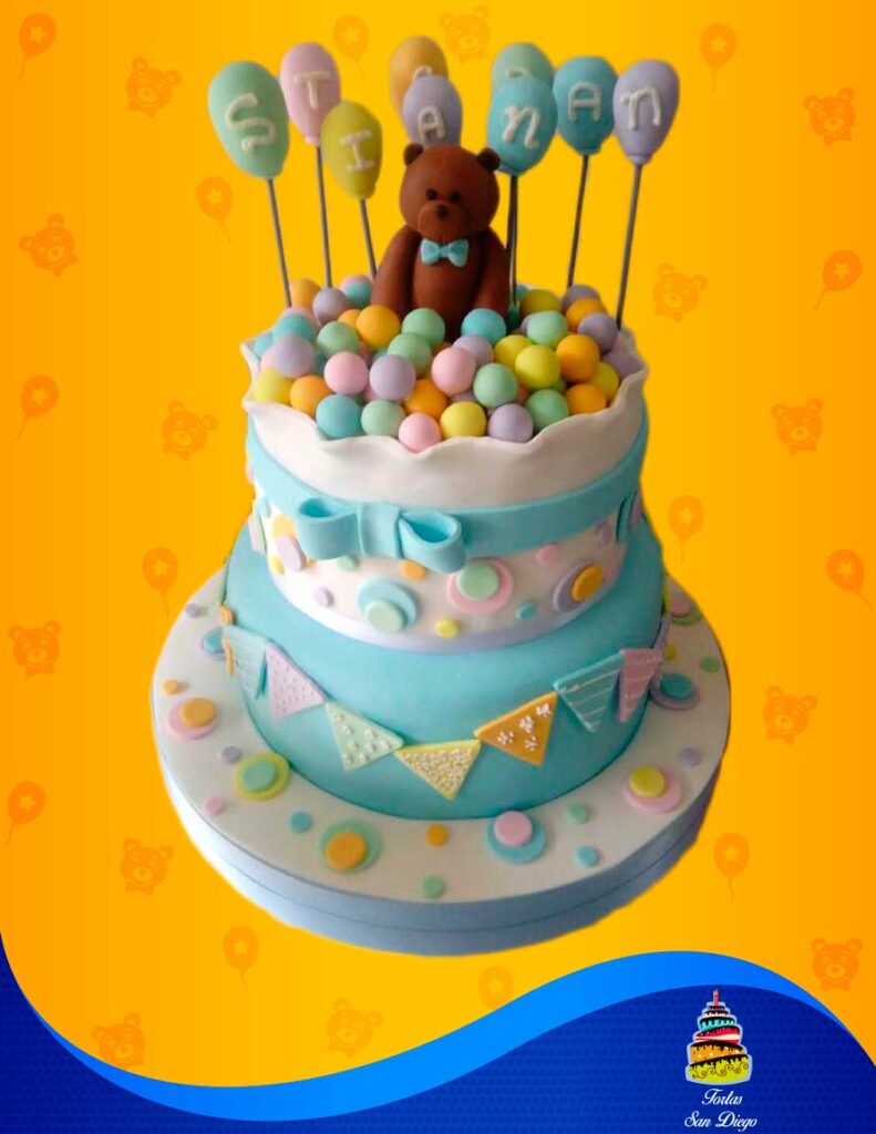 Torta de baby shower con oso, pelotas de fondant y decoraciones en tonos pastel.